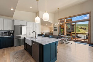 A modern kitchen with a central island, stainless steel appliances, and a dining area with a view of the outdoors. - Sweeping Mountain Views with Private Hot Tub (Silverthorne)