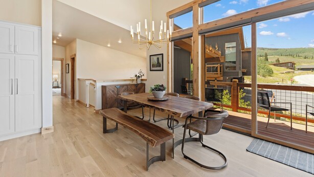 Un amplio comedor con una mesa y bancos de madera, una lámpara de araña y vistas al exterior.