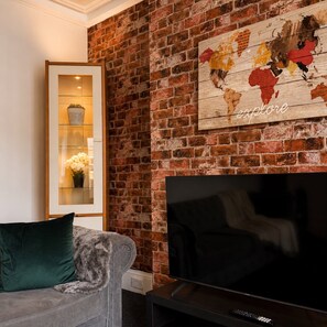 Ein Wohnzimmer mit Backsteinwand, Flachbildfernseher, Sofa und einer Weltkarte als Wandbild.