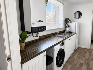 Eine kleine Küche mit integriertem Waschtrockner, Spüle und einem Fenster mit Jalousien.