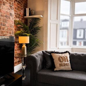 Un salon avec un mur en briques, un canapé avec un coussin, une lampe et un téléviseur.