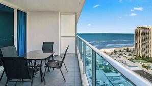 Varanda com mesa e cadeiras, com vista para uma praia e oceano.
