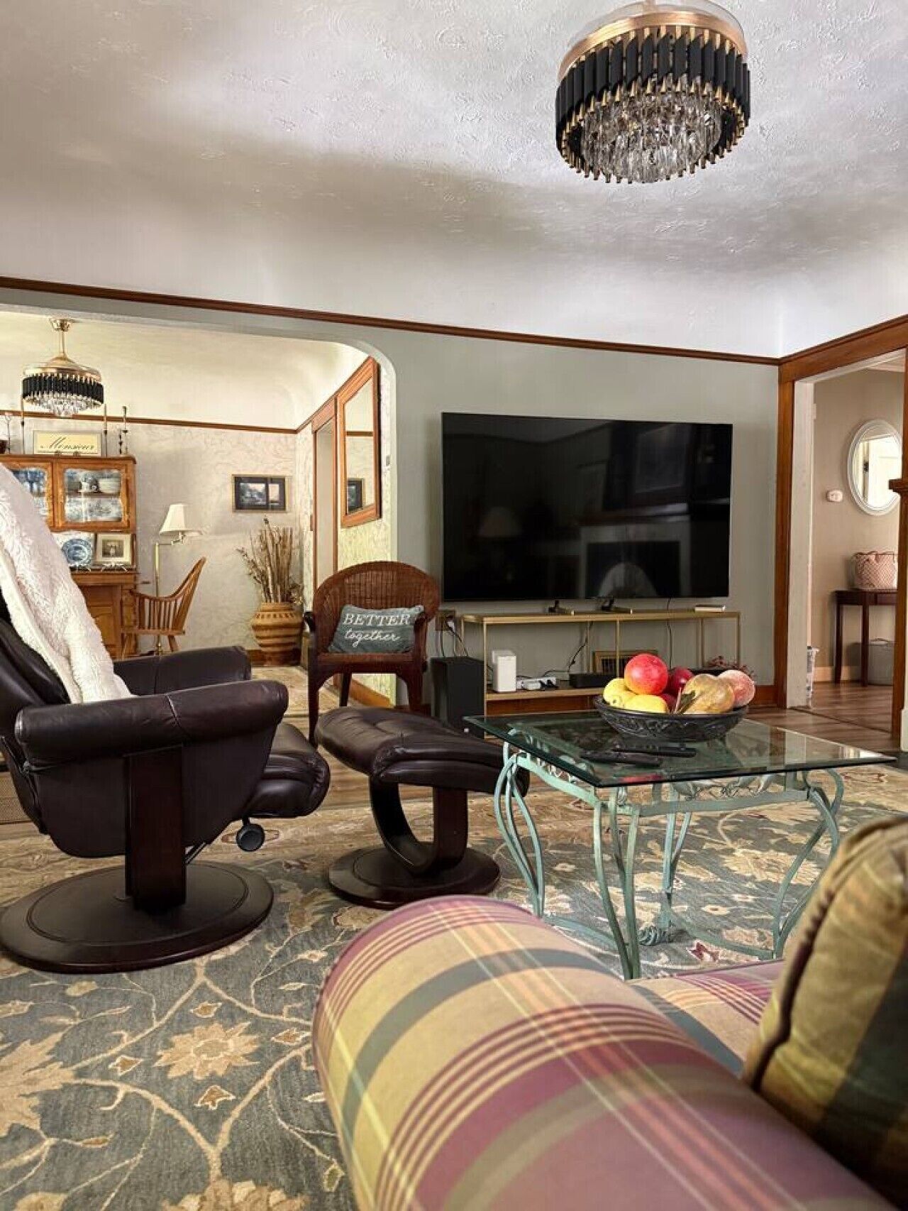 Ein Wohnzimmer mit einer Couch, Sesseln, einem Glastisch, einem Fernseher und einer Chandelier.
