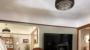 A living room with a sofa, armchairs, a glass coffee table, a TV, and a chandelier. - Elegant & Classic (South Hill Vibes) (Spokane)