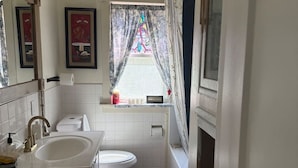 A compact bathroom with a sink, toilet, and bathtub. A window with a stained glass design is visible. - Elegant & Classic (South Hill Vibes) (Spokane)
