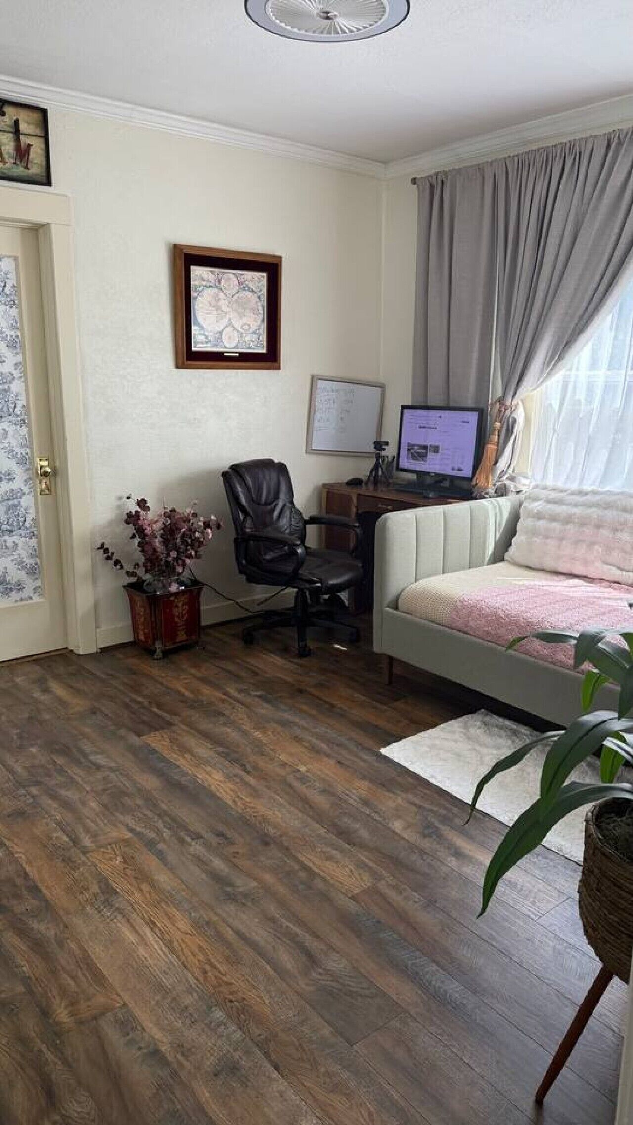 Une pièce comprenant un lit, un bureau avec un ordinateur, une chaise, une plante en pot et un tableau encadré accroché au mur.