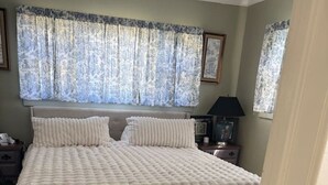 A bedroom with a large bed, a nightstand, a lamp, and a window with curtains. - Elegant & Classic (South Hill Vibes) (Spokane)