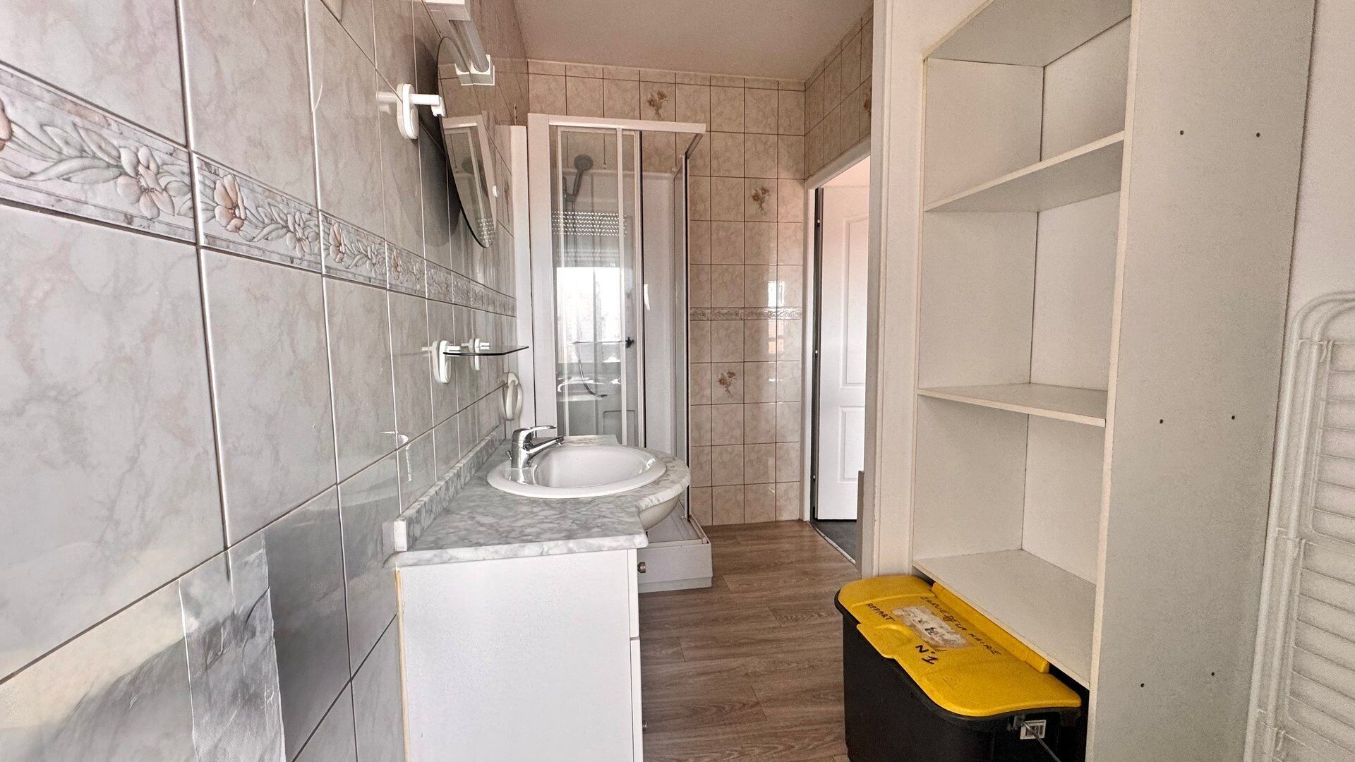Une salle de bain avec une douche, un lavabo et des toilettes. On y trouve une poubelle jaune et un meuble blanc.