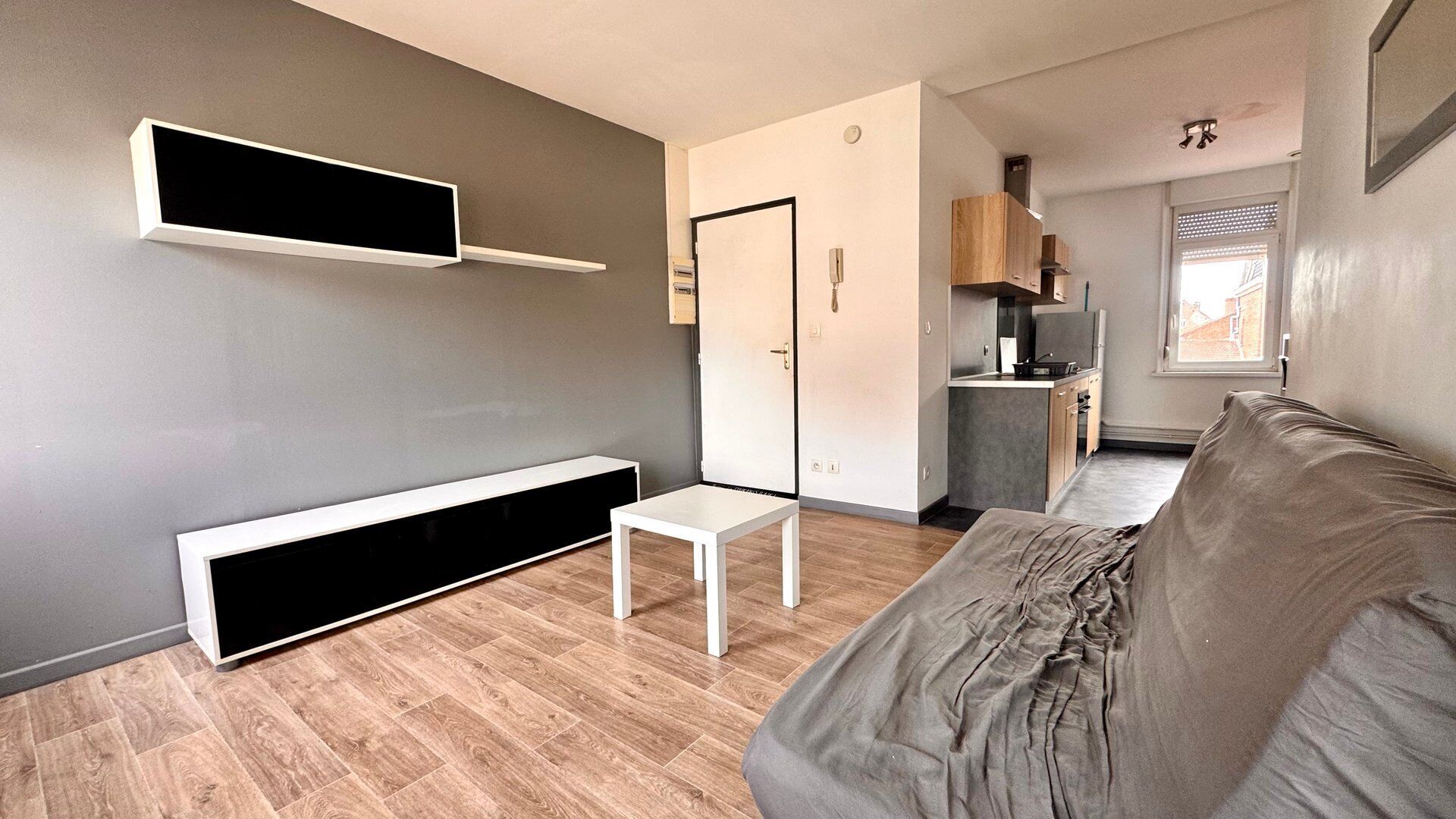 Un salon moderne avec un canapé gris, une table basse blanche et une étagère intégrée pour la télévision.