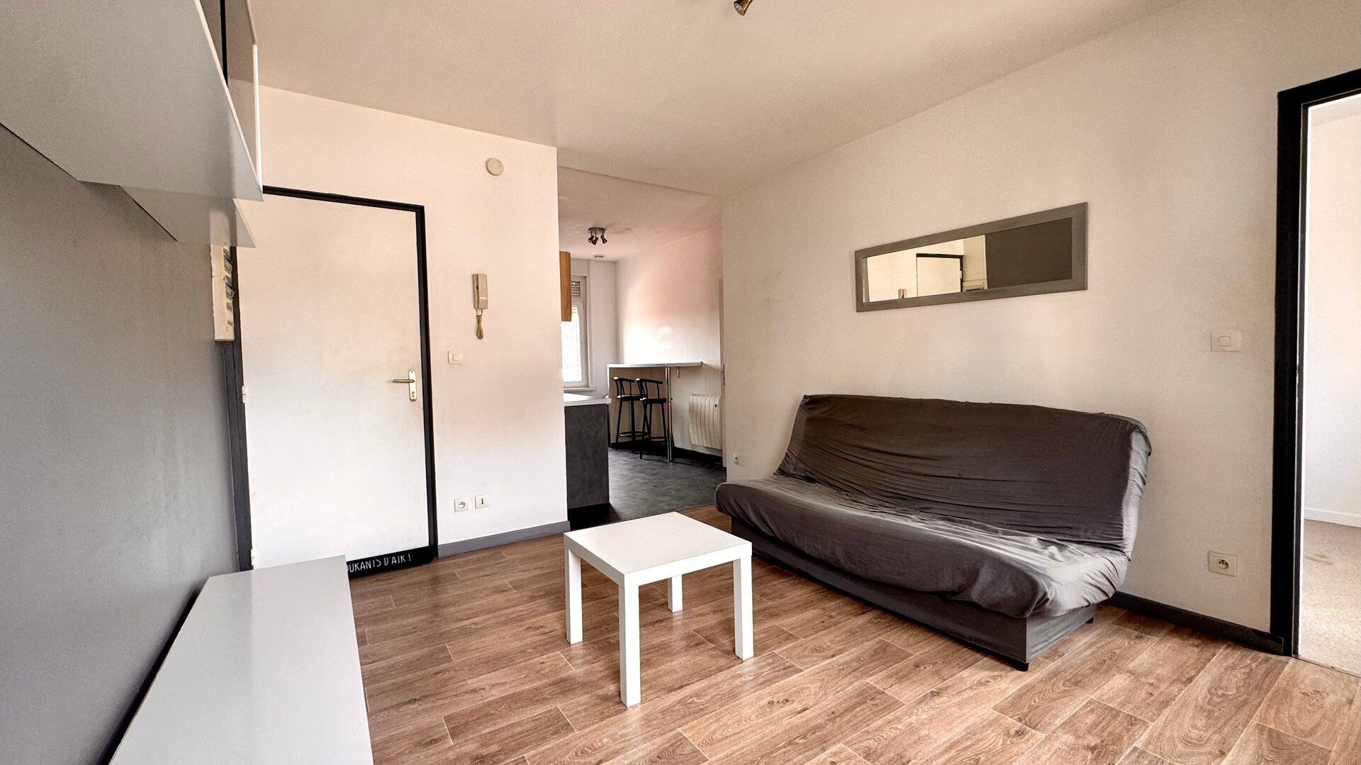 Un espace de vie compact comprenant un canapé, une petite table et un coin cuisine.