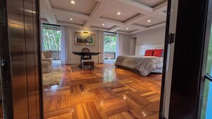 A spacious room with a wooden parquet floor, a bed with red pillows, a desk with a chair, and a painting on the wall. - Villa Casa Blanca (Teresópolis)