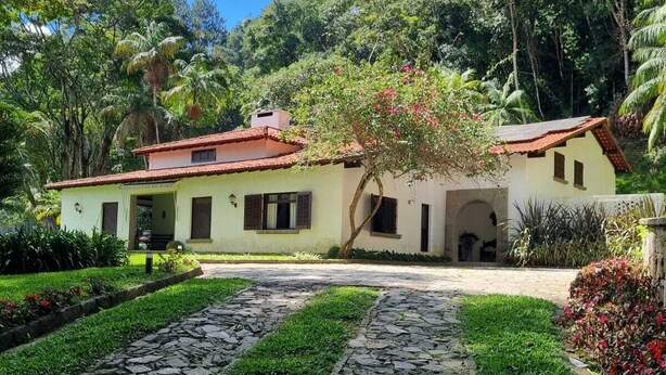 A house with a red-tiled roof, surrounded by lush greenery and a stone pathway leading to the entrance. - Villa Casa Blanca (Teresópolis)