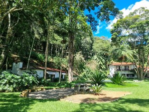 A lush garden with a pathway, a palm tree, and a building with a red roof. - Villa Casa Blanca (Teresópolis)