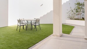 Un patio moderno con un tavolo rotondo e sedie, un piccolo prato e un muro bianco.