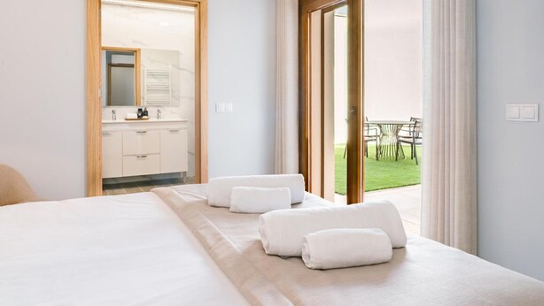Camera d'albergo con un letto, bagno con specchio e vista su una zona verde tramite una porta scorrevole.