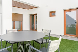 Un espace repas extérieur moderne, doté d’une table ronde et de quatre chaises, d’une petite fenêtre et d’une porte-fenêtre coulissante.