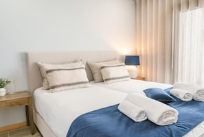 A double bed with two pillows, a bedside table with a lamp, and a window with curtains.