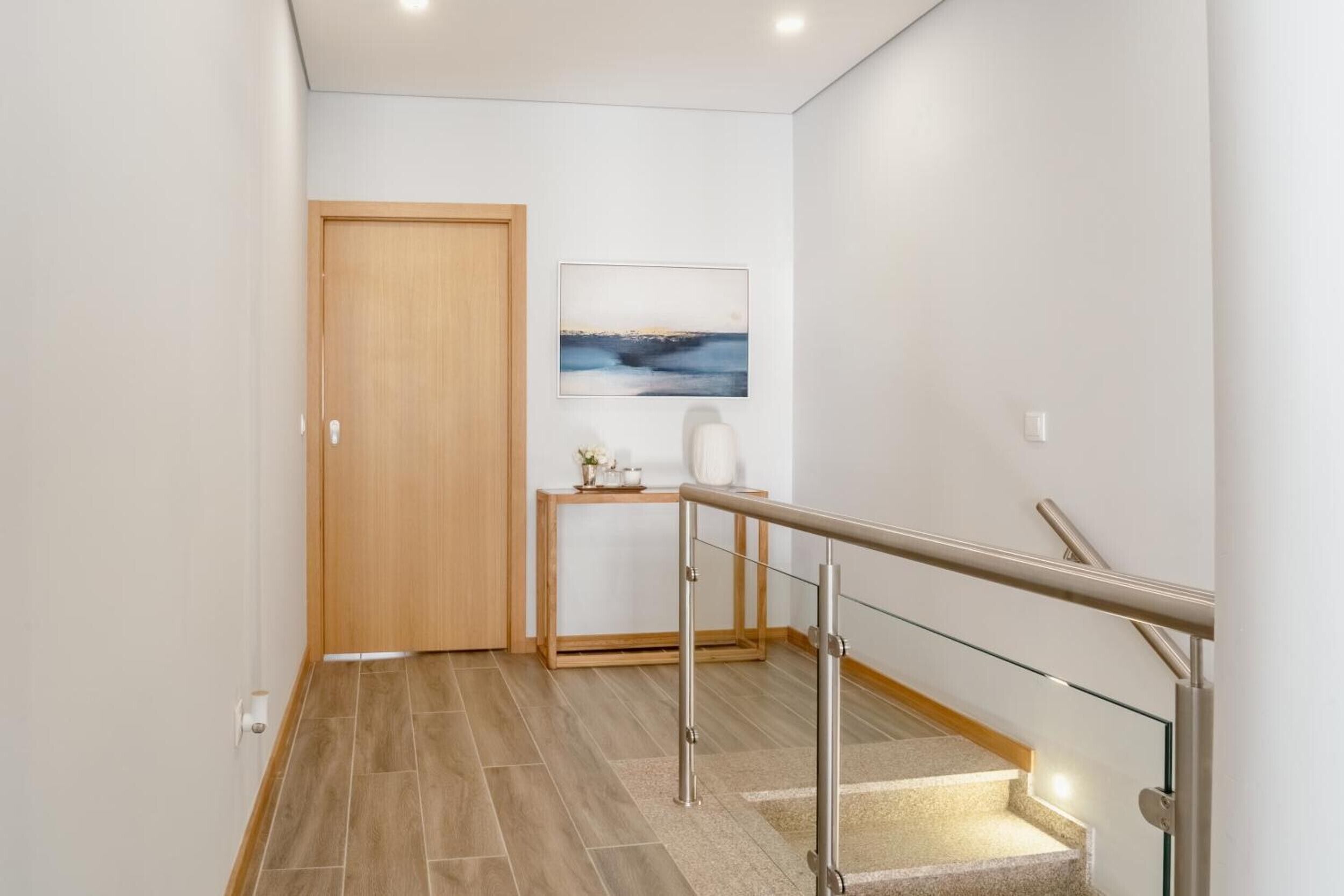 A modern hallway with a wooden door, a small table with a vase, and a painting on the wall.