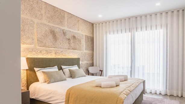 Camera da letto con parete in pietra, un letto grande con molti cuscini, un comodino e una poltrona.
