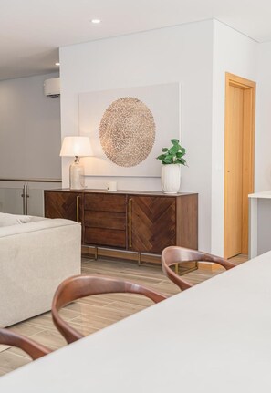 Ein modernes Wohnzimmer mit einer Couch, einem Holz-Fischgrätmuster-Schrank, einem runden Wandbild, einer Lampe und einem Topf mit Pflanze.