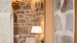 Une pièce aux murs de pierre, avec un banc en bois, une lampe et une petite table.