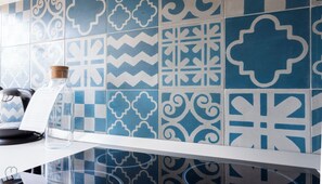 A kitchen with blue and white patterned tiles, a coffee machine, and a clear glass jar on the counter. - Italianway - San Calocero 29 B (Milano)