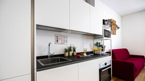 Una cucina moderna con mobili bianchi, un piano di lavoro nero, un lavello in acciaio inossidabile, un forno a microonde e un forno. Sul piano di lavoro si trova una sedia rossa e una piccola pianta.