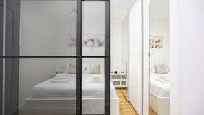A modern, minimalist bedroom with a large bed, a walk-in closet, and a mirrored wardrobe. - Italianway Comfort - Boncompagni 3B (Milan)