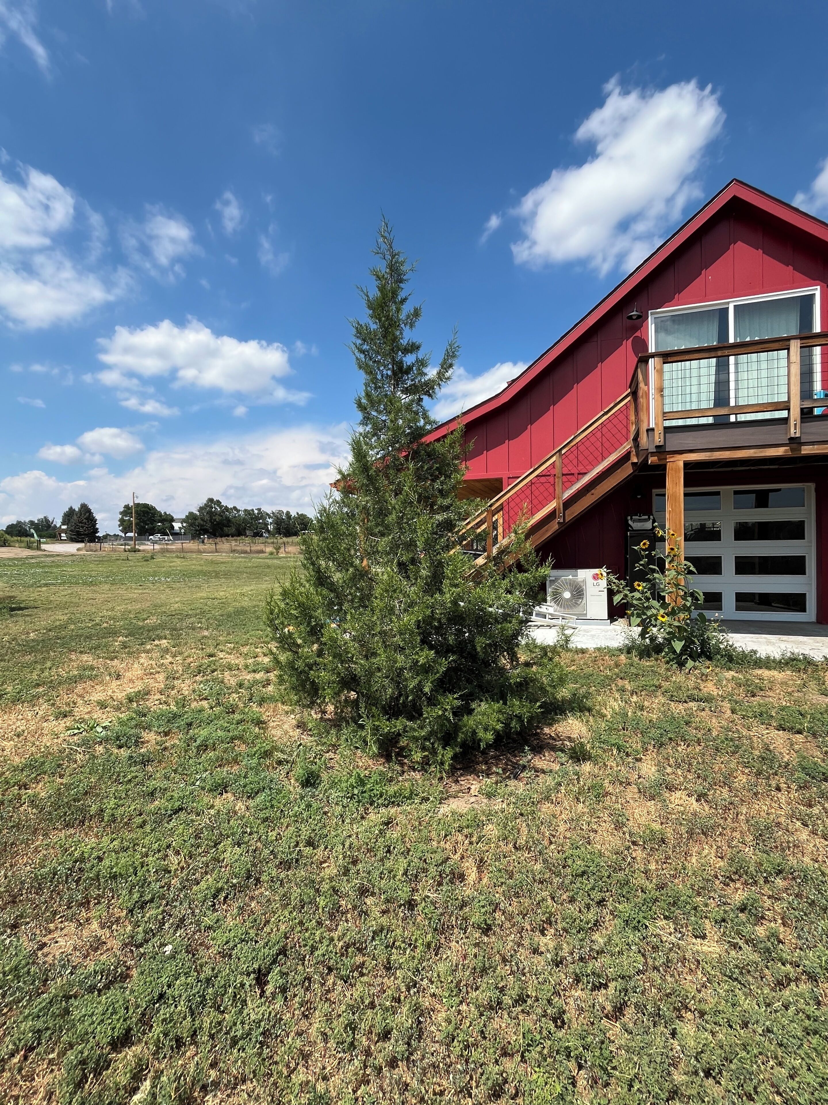 A red building with a balcony, a small tree, and a grassy field.