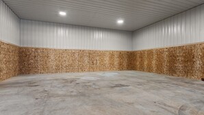 Um espaço amplo e vazio com piso de concreto e paredes de painéis de madeira, destacando-se por um alto teto e iluminação embutida.