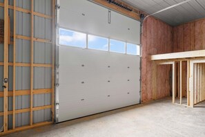 A garage with a large white door, wooden framing, and a concrete floor. - Cozy 1-bedroom barn in lovely Seattle with AC (Seattle)