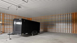 Uma trailer preta em um armazém com paredes de metal corrugado e piso de concreto.