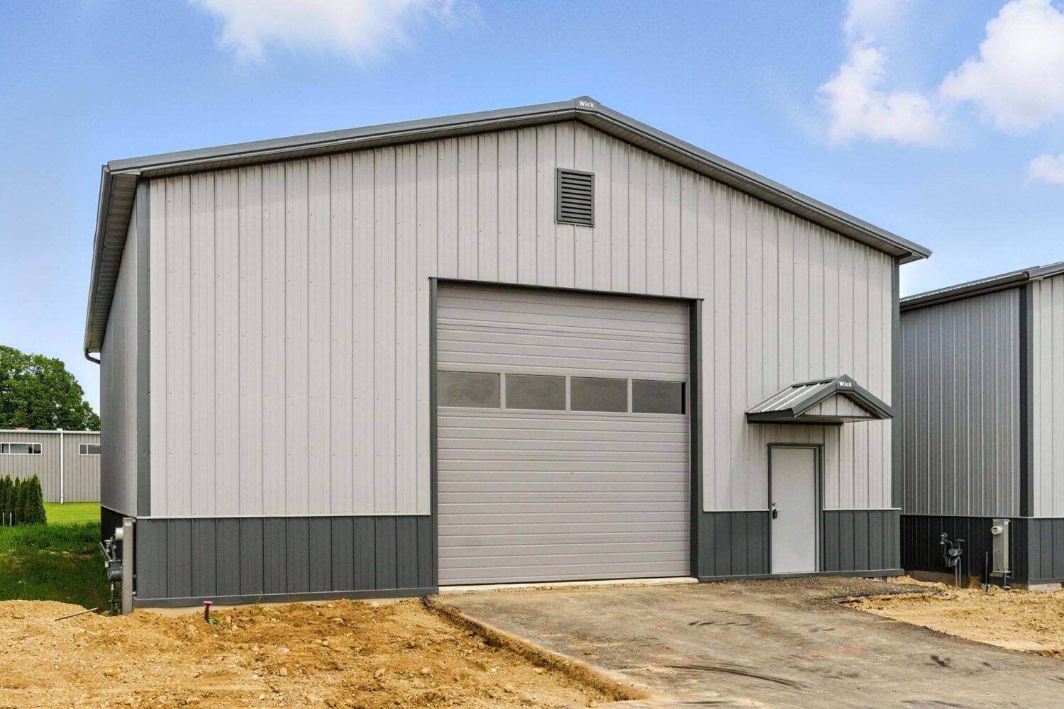 A large industrial building with a grey metal exterior, a large garage door, and a small door on the side.