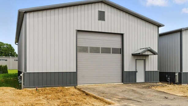 Um grande edifício industrial com fachada de metal cinzento, uma porta de garagem ampla e uma pequena porta lateral.