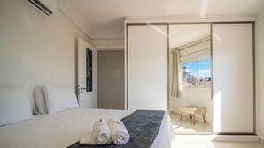 Una camera d'albergo con un letto, una porta del bagno, un balcone con vista e un piccolo sgabello.