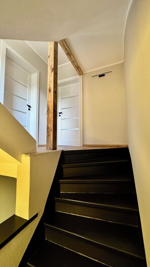 Eine Treppe mit schwarzen Stufen, Holzbalken und weißen Türen.