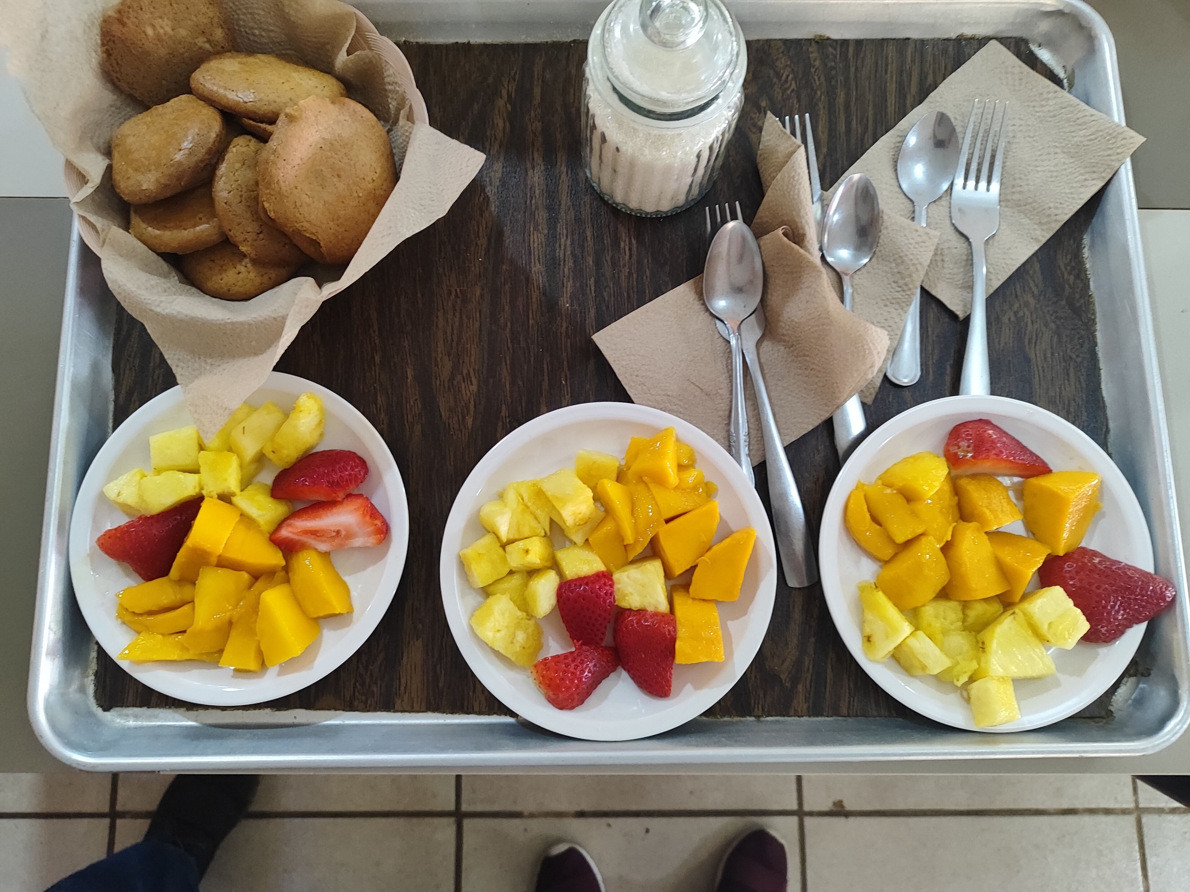 A tray with three plates of fruit, a basket of cookies, and a jar of milk.