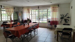 A dining area with tables and chairs, a refrigerator, and windows with curtains. - el jardin de los anturios (Xico)
