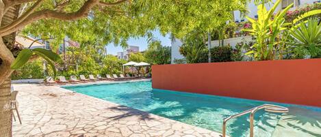 A swimming pool with stone tiles, lounge chairs, and a red wall.
