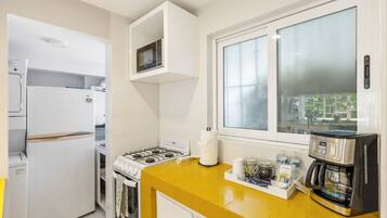 Une cuisine moderne équipée d’une cuisinière à gaz, d’appareils électroménagers blancs, d’un plan de travail jaune et d’une machine à café.