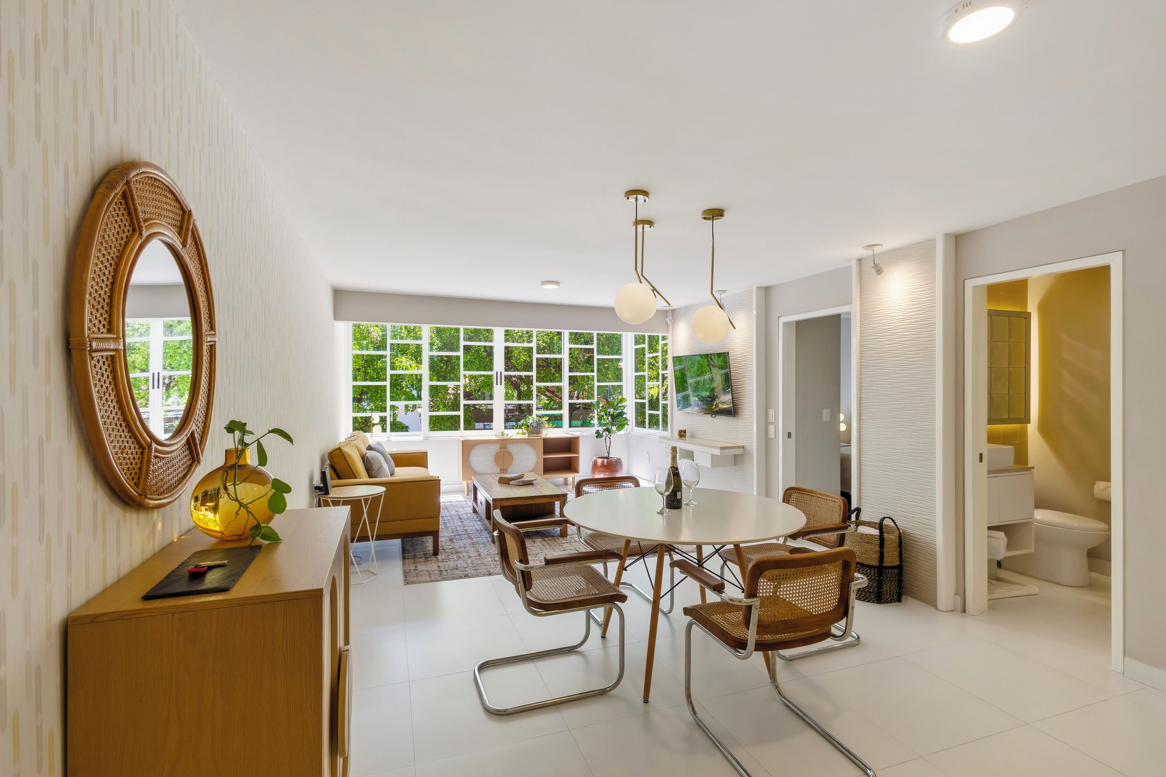 A modern living room with a dining area, large windows, and a view of greenery.