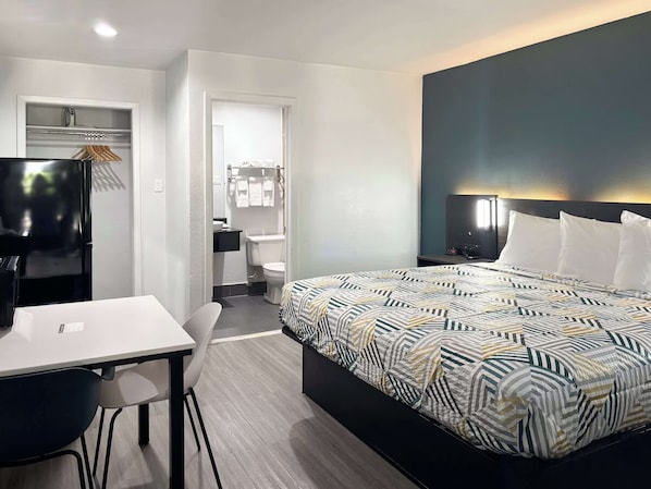 Una habitación de hotel moderna con una cama, un escritorio, una silla, un armario y un baño.
