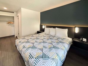 Una habitación de hotel con una cama grande, una mesita de noche, una lámpara de pared y un armario con perchero.