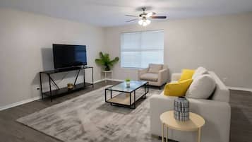 A living room with a TV, sofa, coffee table, and a ceiling fan.