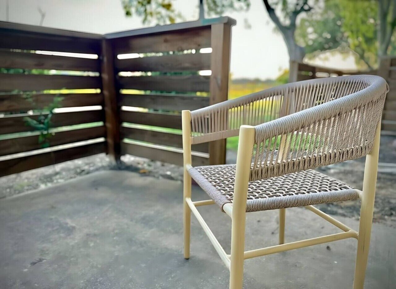 A wicker chair with a metal frame, positioned outdoors with a wooden fence in the background.