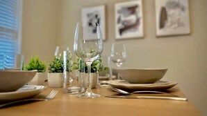 Una mesa de comedor dispuesta con platos, tazones, cubiertos y vasos, con plantas en macetas y cuadros en la pared.