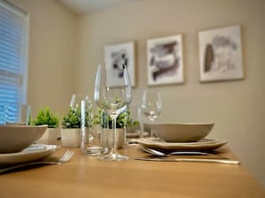 A dining table set with plates, bowls, cutlery, and glasses, with potted plants and framed pictures on the wall.