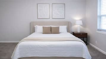 A bedroom with a bed, a ceiling fan, a nightstand with a lamp, and abstract art on the wall.