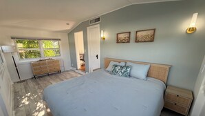 Ein Schlafzimmer mit einem großen Bett, Nachttischen, einer Kommode, einem Fenster und einer Tür zu einem anderen Raum.