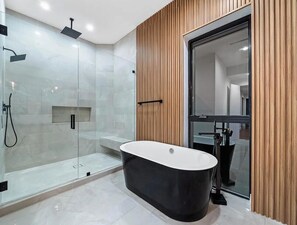 Ein modernes Badezimmer mit freistehender Badewanne, einer gläsernen Duschkabine und einer Wandverkleidung aus Holz.